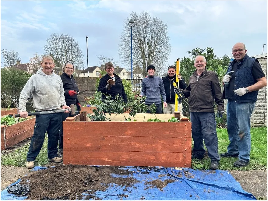 A group of people stood round a planter box that they have repaired